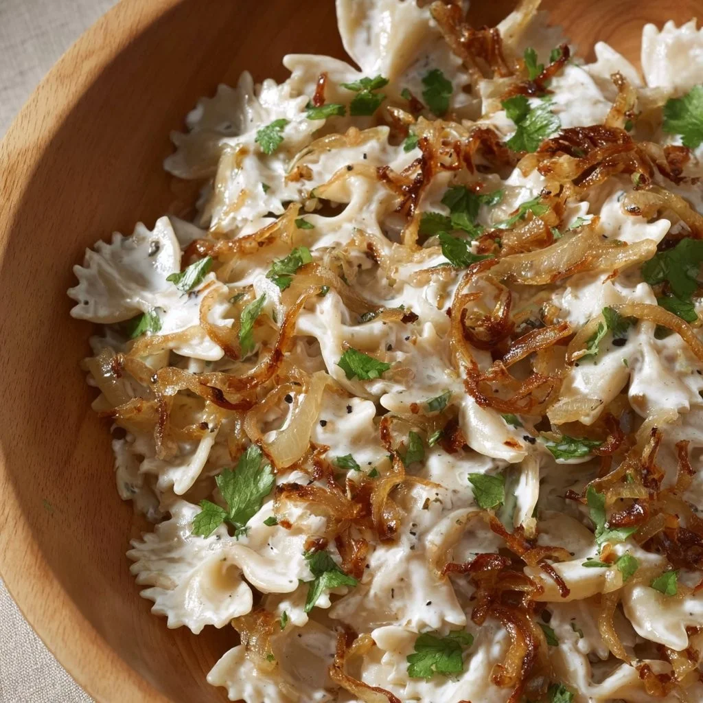 Bowl of French onion pasta salad garnished with herbs and cheese.